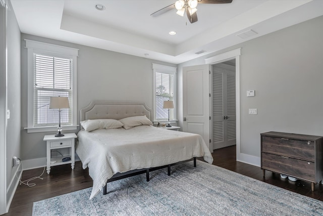 bedroom with dark hardwood / wood-style flooring, a raised ceiling, and ceiling fan