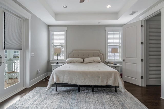 bedroom with multiple windows, dark hardwood / wood-style floors, and a tray ceiling