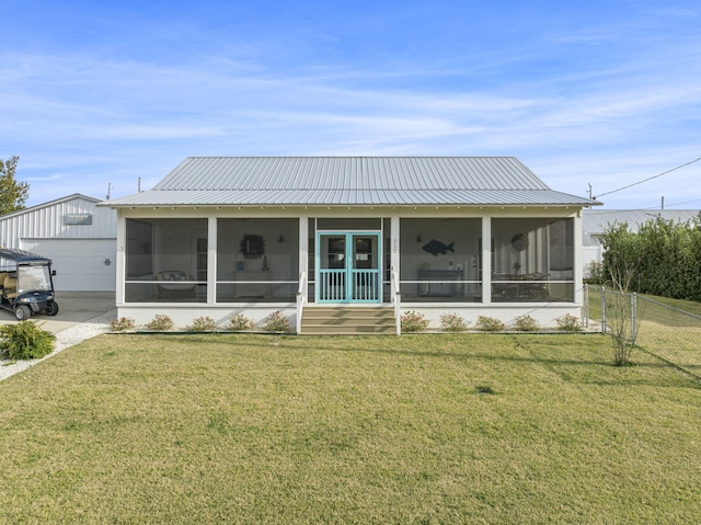 back of house featuring a sunroom, a garage, an outbuilding, and a lawn