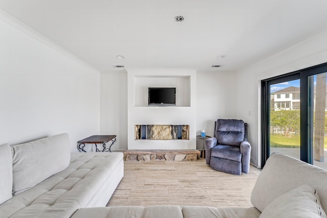 living room featuring crown molding, a stone fireplace, and light hardwood / wood-style floors