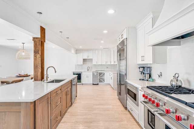 kitchen with a kitchen island with sink, hanging light fixtures, white cabinets, premium appliances, and premium range hood