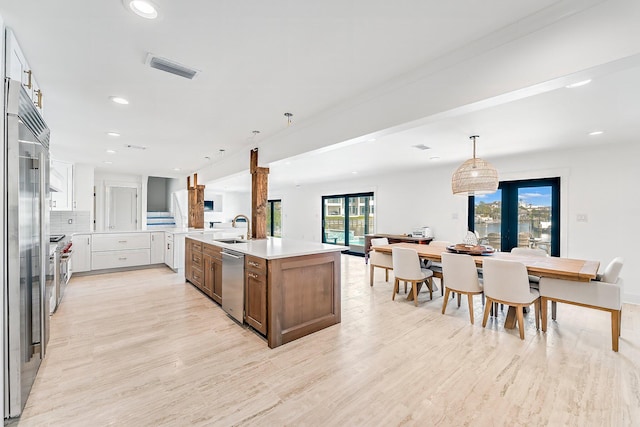 kitchen with backsplash, hanging light fixtures, white cabinetry, light hardwood / wood-style floors, and a kitchen island with sink