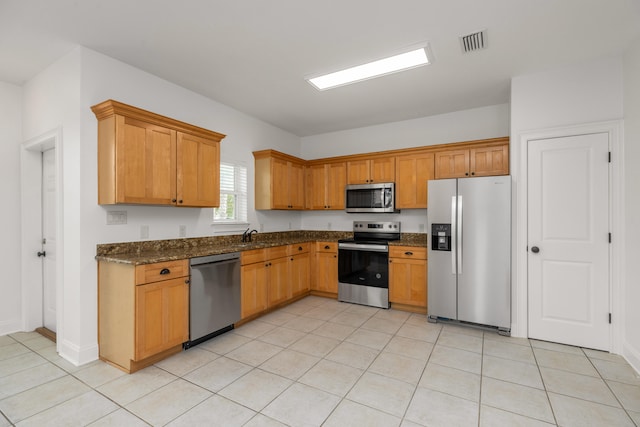 kitchen with light tile patterned flooring, appliances with stainless steel finishes, and dark stone counters