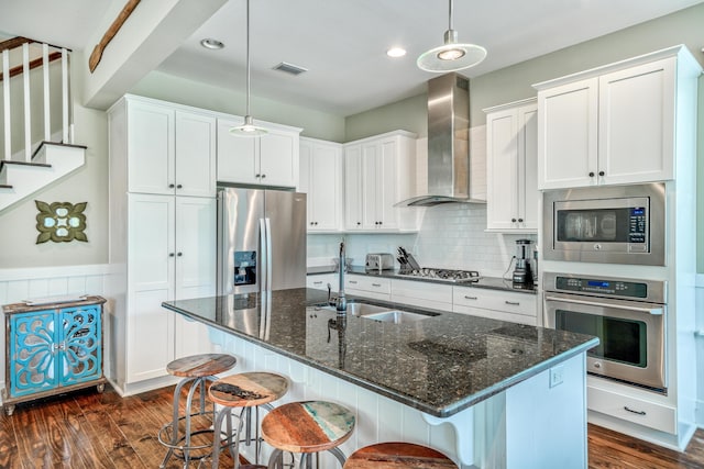 kitchen with an island with sink, white cabinetry, dark wood-type flooring, wall chimney exhaust hood, and stainless steel appliances