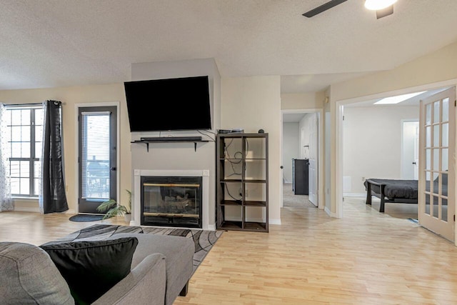 living room with ceiling fan, a textured ceiling, and light hardwood / wood-style flooring