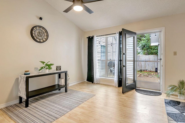 doorway to outside featuring light wood-type flooring, lofted ceiling, a textured ceiling, and ceiling fan