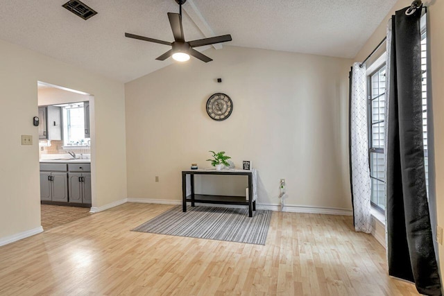 interior space featuring lofted ceiling, a textured ceiling, sink, ceiling fan, and light wood-type flooring