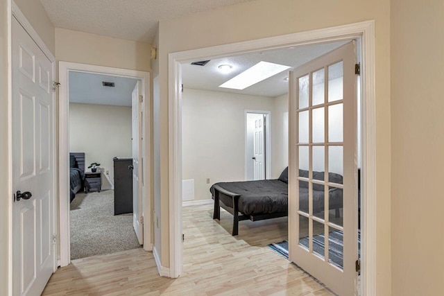 corridor featuring light wood-type flooring, a textured ceiling, and a skylight