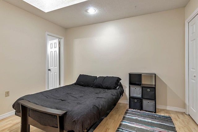 bedroom featuring light hardwood / wood-style floors, a textured ceiling, and a skylight