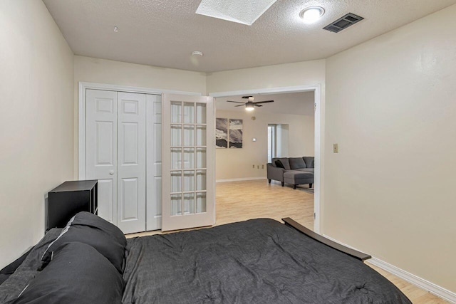 bedroom featuring ceiling fan, a textured ceiling, light wood-type flooring, and a skylight