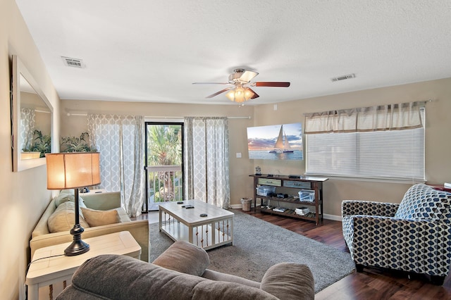 living room featuring dark wood-type flooring, ceiling fan, and a textured ceiling