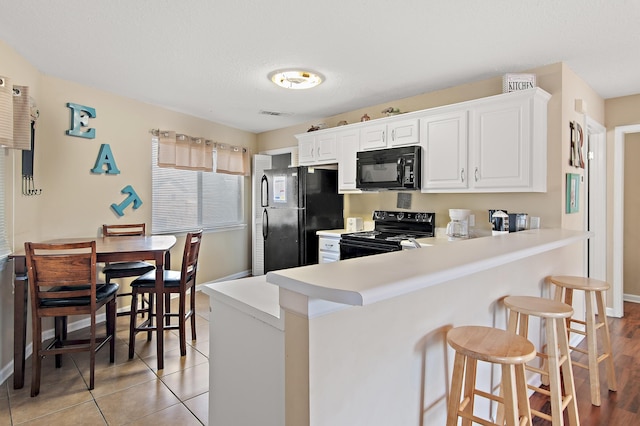 kitchen featuring black appliances, kitchen peninsula, light hardwood / wood-style floors, white cabinets, and a breakfast bar area