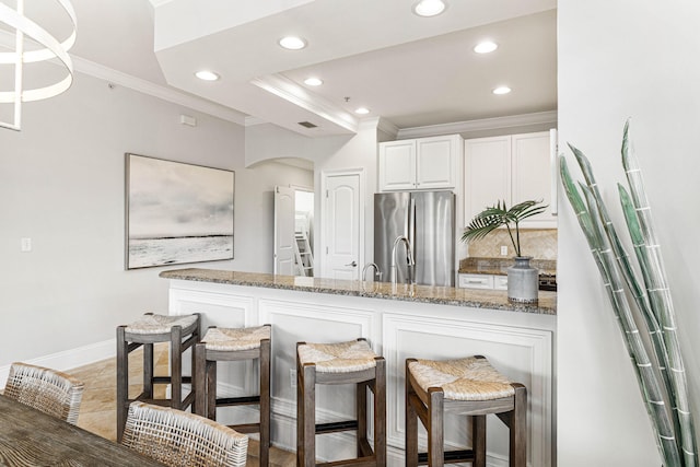 kitchen featuring stainless steel refrigerator, white cabinetry, backsplash, dark stone counters, and ornamental molding