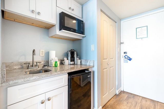 kitchen featuring light stone countertops, black appliances, sink, white cabinets, and light hardwood / wood-style flooring