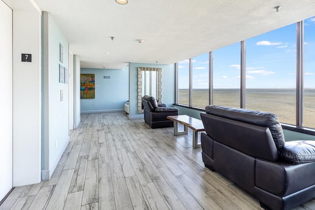 living room featuring a textured ceiling, a water view, light hardwood / wood-style floors, and floor to ceiling windows