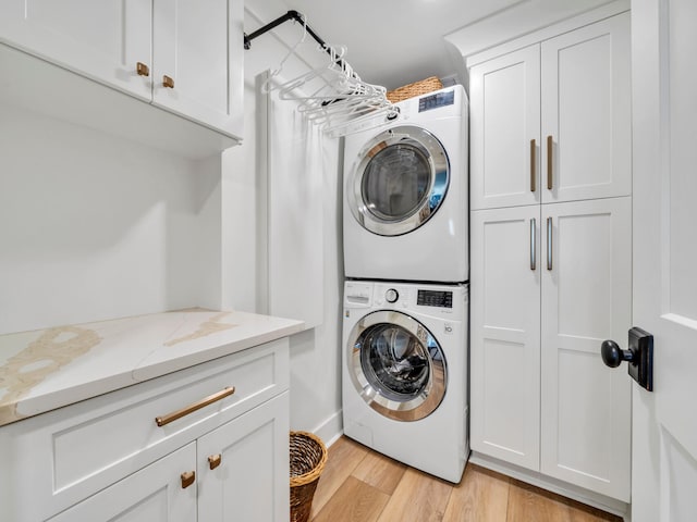 laundry area with stacked washing maching and dryer, light hardwood / wood-style floors, and cabinets