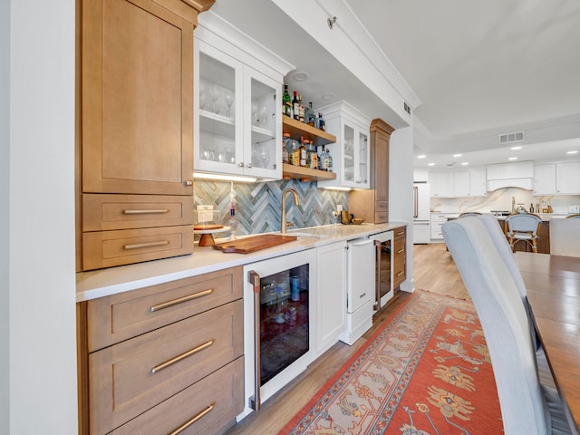 bar with white cabinets, light hardwood / wood-style flooring, beverage cooler, and white fridge