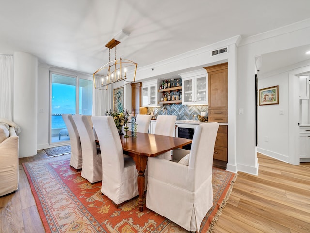 dining area with a chandelier, ornamental molding, and light hardwood / wood-style flooring