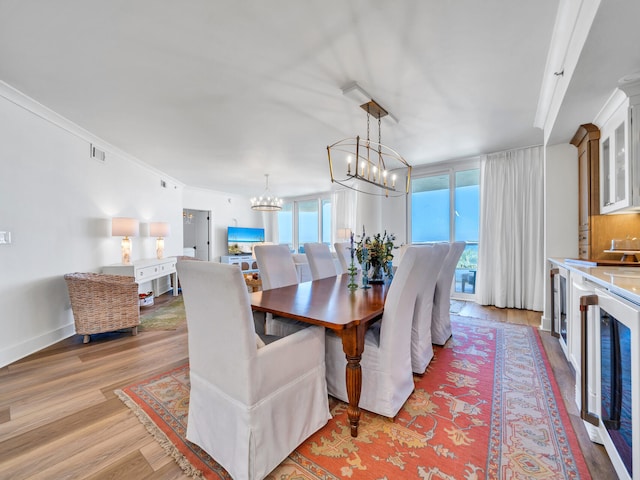 dining space featuring light wood-type flooring, beverage cooler, a notable chandelier, and crown molding