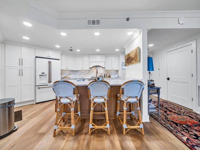 kitchen featuring white cabinetry, a kitchen breakfast bar, light hardwood / wood-style floors, kitchen peninsula, and high end fridge