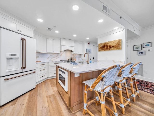 kitchen featuring backsplash, white cabinets, a kitchen breakfast bar, light hardwood / wood-style floors, and white appliances