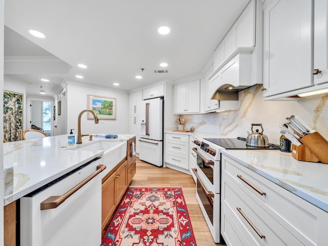 kitchen with white cabinets, white appliances, light stone countertops, and light wood-type flooring