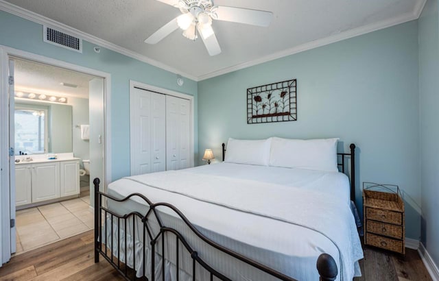 bedroom featuring ensuite bath, ornamental molding, ceiling fan, wood-type flooring, and a closet