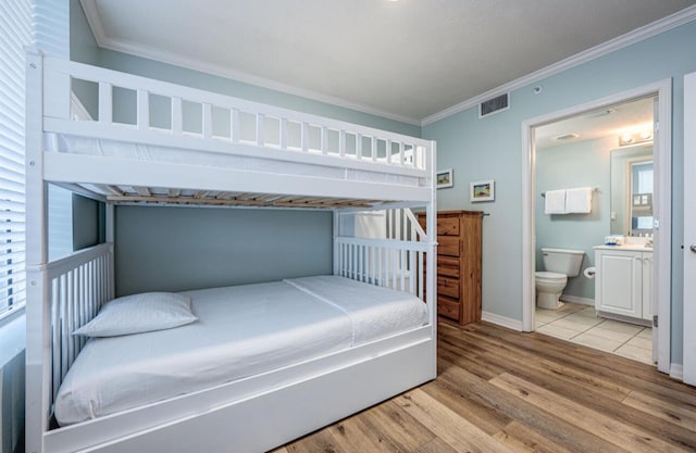 bedroom featuring ensuite bath, light hardwood / wood-style flooring, and crown molding