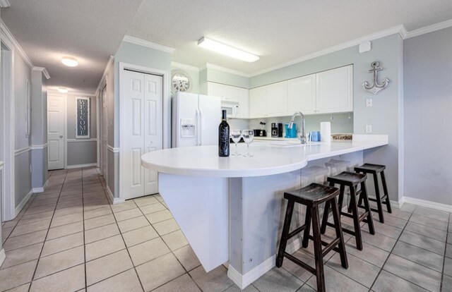 kitchen with a kitchen bar, white cabinets, kitchen peninsula, crown molding, and white appliances