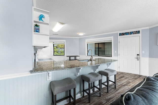 kitchen featuring light stone counters, ornamental molding, sink, a breakfast bar, and dark wood-type flooring