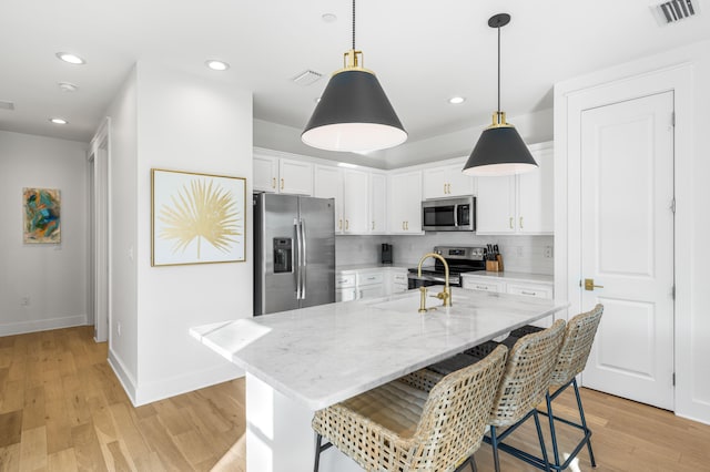 kitchen featuring a center island with sink, stainless steel appliances, decorative backsplash, light hardwood / wood-style floors, and white cabinets