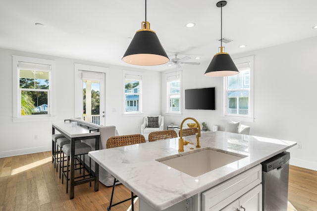 kitchen featuring light wood-type flooring, sink, white cabinets, stainless steel dishwasher, and a kitchen island with sink