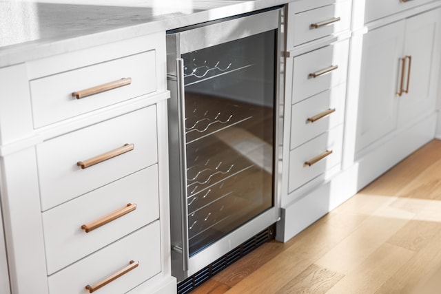 details featuring white cabinets, light hardwood / wood-style flooring, light stone counters, and beverage cooler