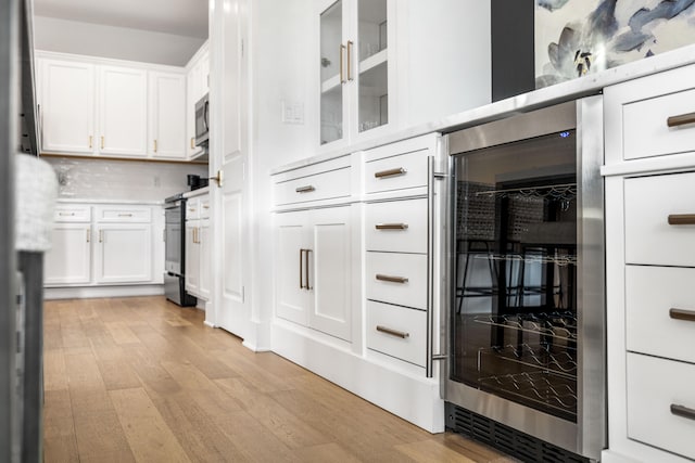 kitchen featuring white cabinetry, wine cooler, appliances with stainless steel finishes, tasteful backsplash, and light hardwood / wood-style flooring