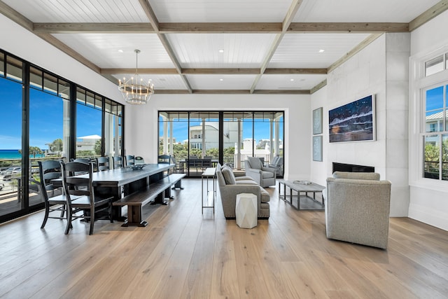 interior space with an inviting chandelier, beamed ceiling, a tile fireplace, and light hardwood / wood-style floors