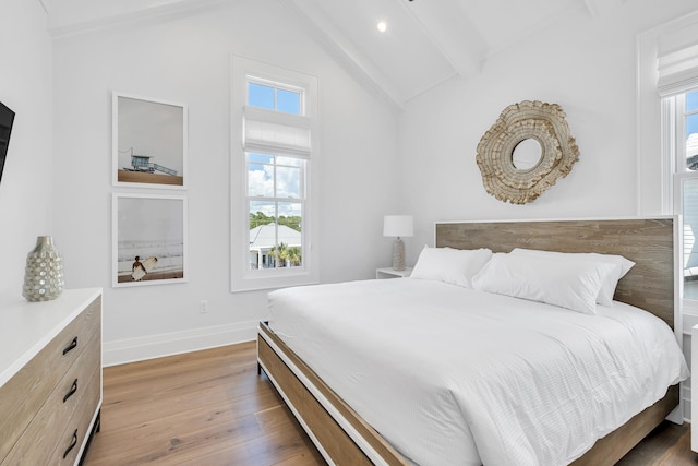 bedroom with multiple windows, vaulted ceiling with beams, and hardwood / wood-style floors