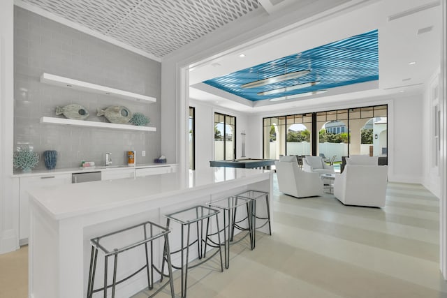 kitchen with decorative backsplash, white cabinets, a tray ceiling, and a kitchen bar