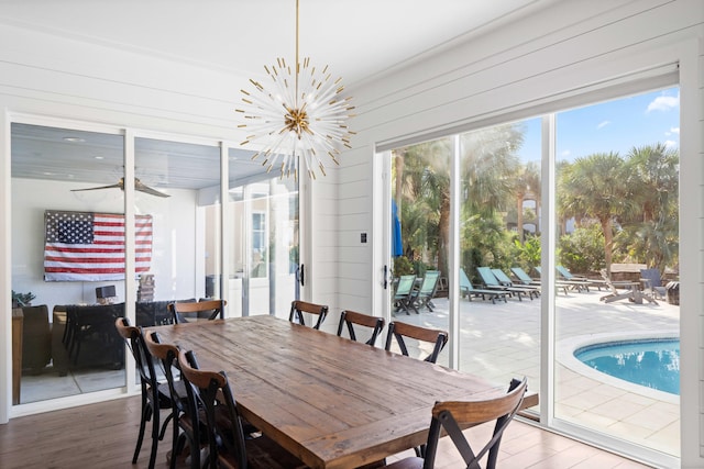 dining space with hardwood / wood-style floors, ceiling fan with notable chandelier, and wood walls