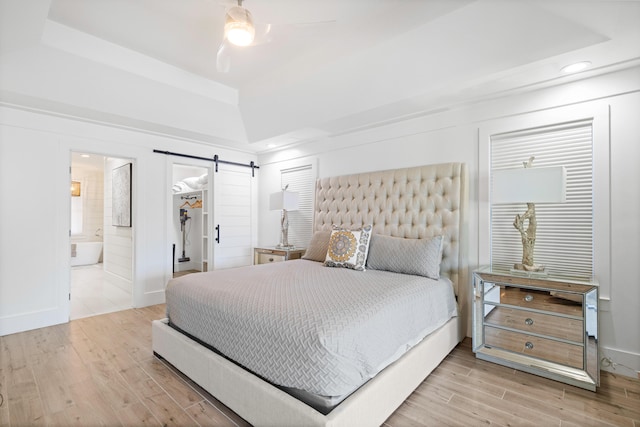 bedroom with hardwood / wood-style flooring, ensuite bath, a barn door, and ceiling fan