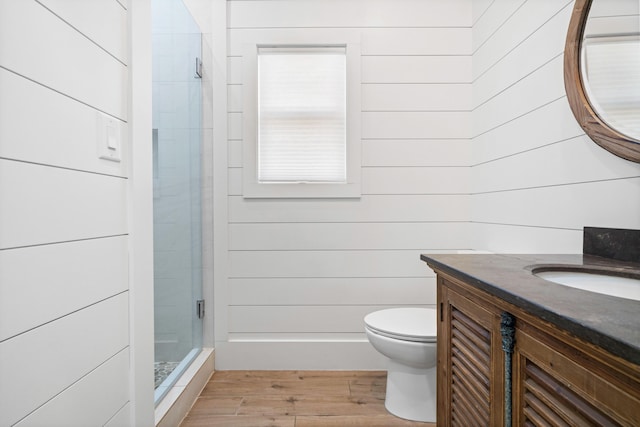 bathroom featuring wood walls, a shower with door, wood-type flooring, vanity, and toilet