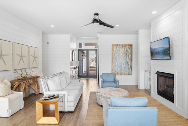 living room with a fireplace, light hardwood / wood-style flooring, wooden walls, and ceiling fan