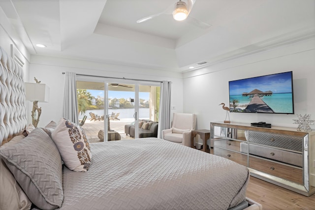 bedroom featuring access to exterior, light hardwood / wood-style flooring, ceiling fan, and a raised ceiling