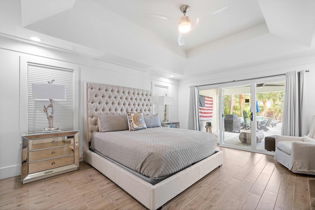 bedroom featuring access to outside, a raised ceiling, ceiling fan, and light wood-type flooring