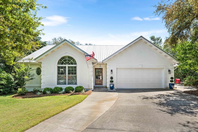 ranch-style home with asphalt driveway, metal roof, a front yard, and stucco siding