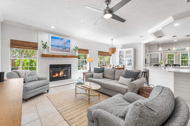 living area featuring a ceiling fan, a large fireplace, light tile patterned floors, plenty of natural light, and a textured ceiling
