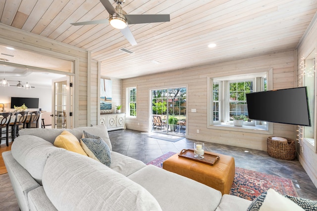 living area featuring wooden walls, healthy amount of natural light, wooden ceiling, and ceiling fan