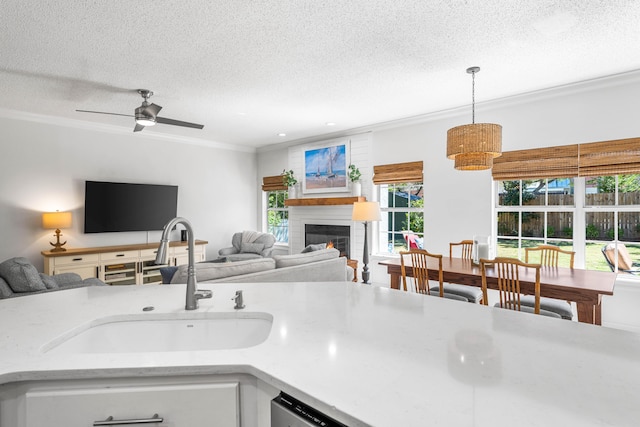 kitchen featuring hanging light fixtures, a textured ceiling, sink, ornamental molding, and a fireplace