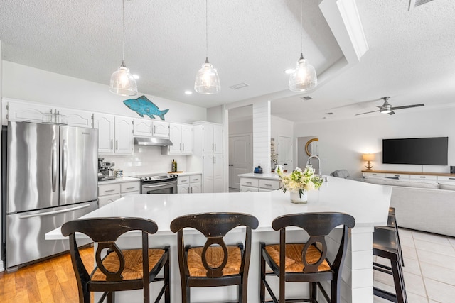 kitchen featuring stainless steel appliances, a textured ceiling, under cabinet range hood, a kitchen bar, and white cabinets