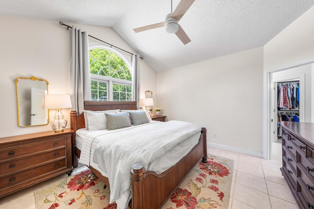 tiled bedroom featuring a closet, a spacious closet, a textured ceiling, vaulted ceiling, and ceiling fan