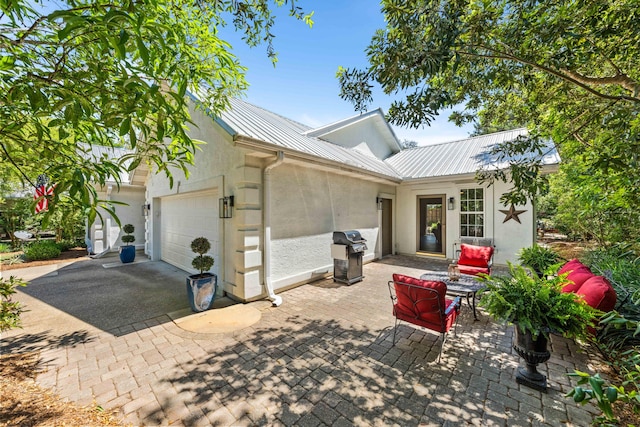 back of property featuring stucco siding, an attached garage, metal roof, and driveway